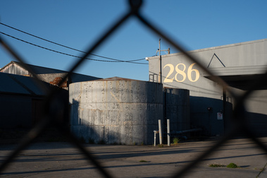 looking through a steel mesh fence to a huge concrete tank and concrete building with pipes and a number '286' and blue sky