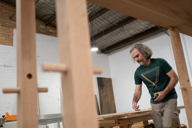 a man holding a tool and feeling the smoothness of the furniture he is sanding, seen through a shelving structure he's building