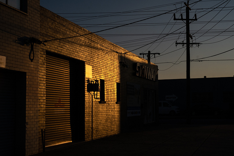 the brick wall of a 1950's factory with a roller door and power lines and late afternoon sky