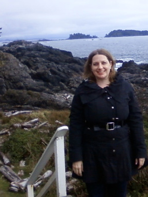 The author is pictured on a rocky coastal path, smiling in a black coat.  The photo was taken in the BC town of Ucluelet on the Westernmost side of Vancouver Island, near its iconic lighthouse, in 2010.