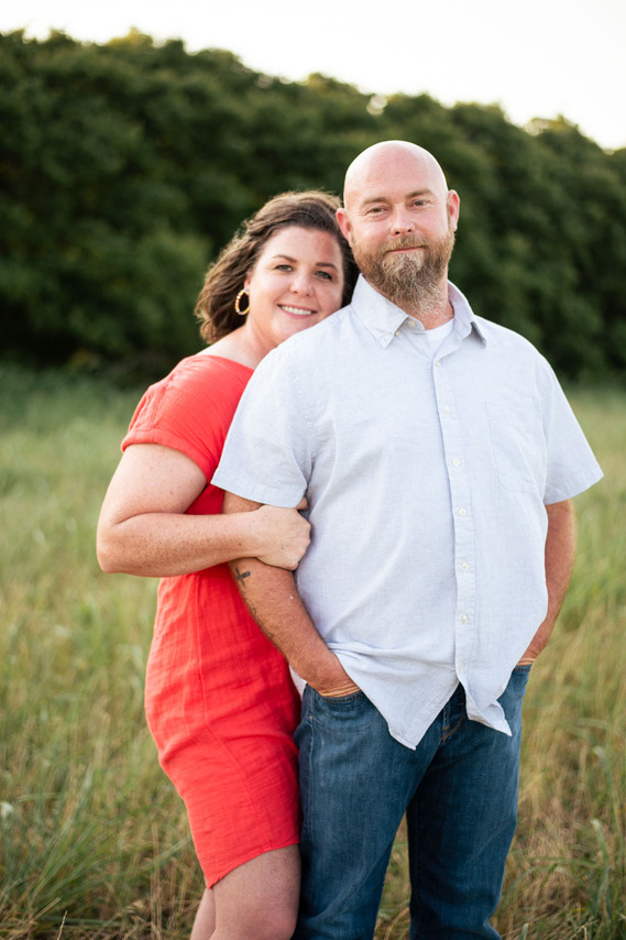 A husband and wife pose in front of a grassy meadow at sunset in Oklahoma