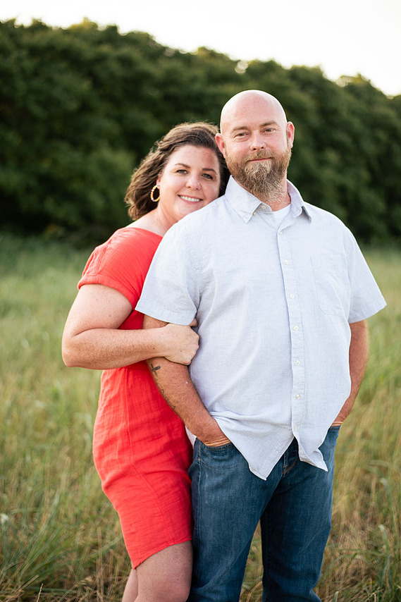 A husband and wife pose in front of a grassy meadow at sunset in Oklahoma