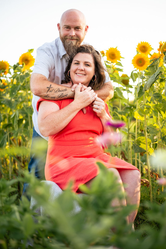 A husband and wife pose in front of a flower meadow at sunset in Oklahoma