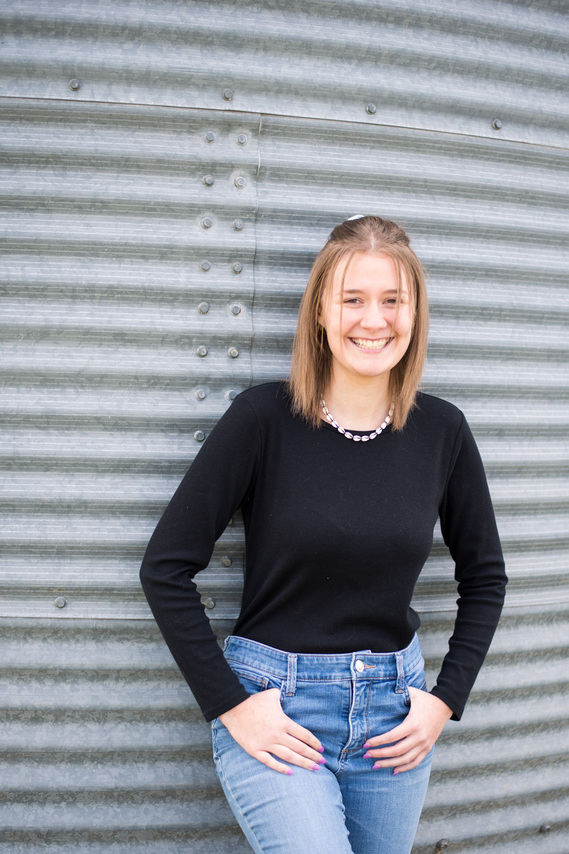portrait of a teenage girl in a black shirt standing in front of a grain bin with a smile