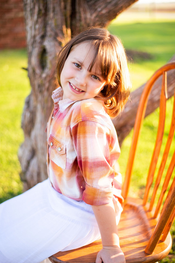A little girl smiles while sitting in a chair at her back to school photo session in the country in Oklahoma