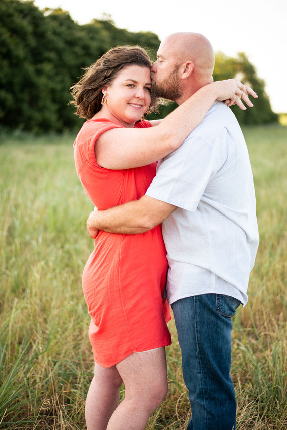 A husband and wife pose in front of a grassy meadow at sunset in Oklahoma
