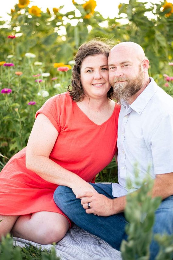 A husband and wife pose in front of a flower meadow at sunset in Oklahoma