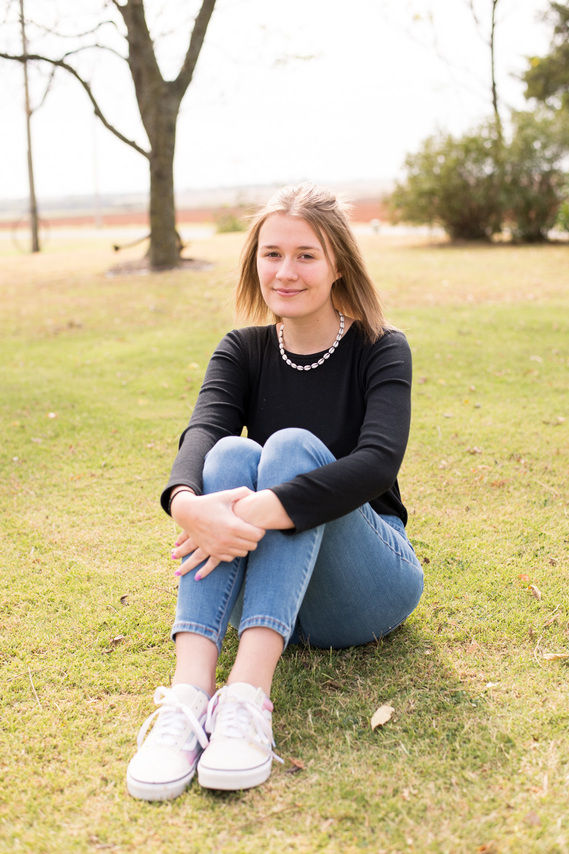 portrait of a teenage girl sitting in the grass with her hands around her knees