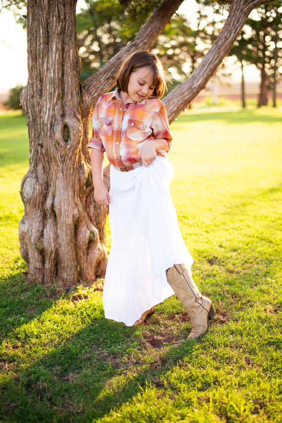 A little girl in her cowgirl outfit looks down at her cowboy boots at her back to school photo session in the country in Oklahoma
