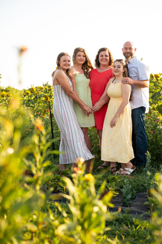Parents and their three teenage daughters pose in front of a flower meadow at sunset in Oklahoma