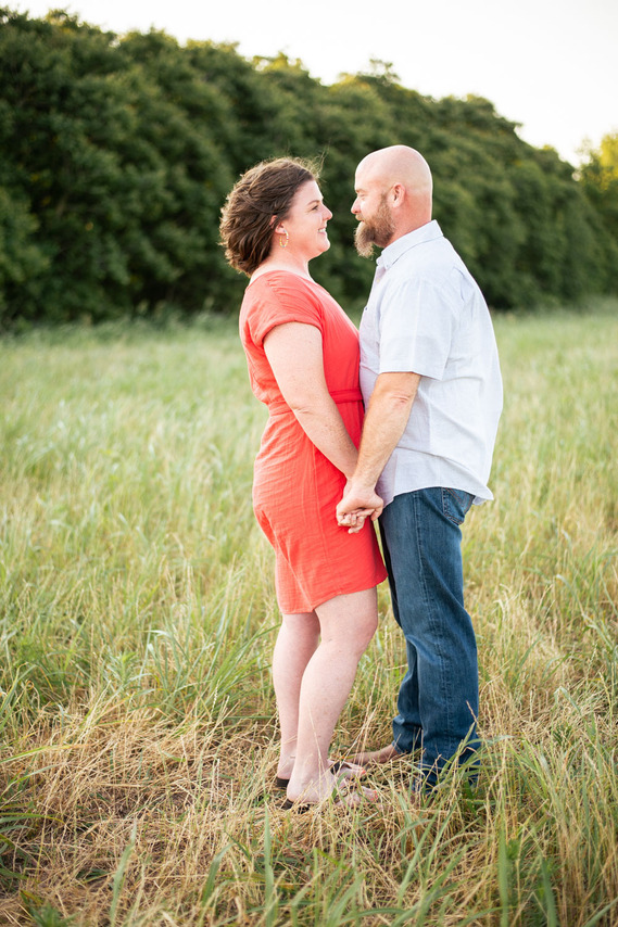 A husband and wife pose in front of a grassy meadow at sunset in Oklahoma