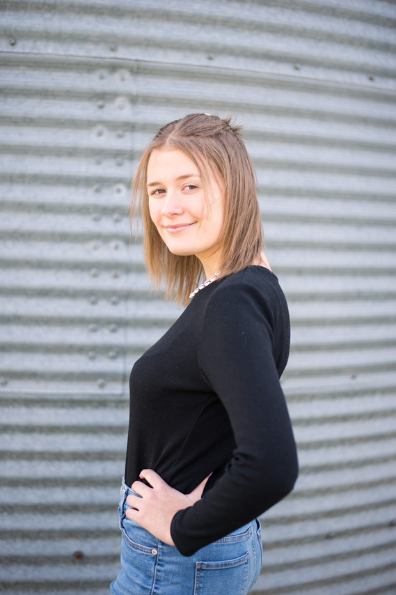Portrait of a teenage girl in a black shirt standing in front of a grain bin looking over her shoulder with her hand on her hip