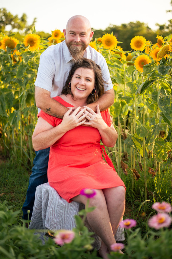 A husband and wife pose in front of a flower meadow at sunset in Oklahoma