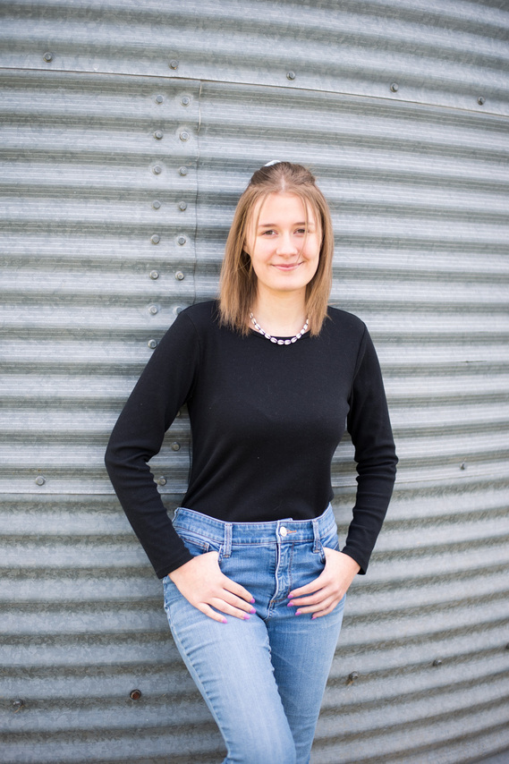 portrait of a teenage girl in front of a grain bin with her thumbs in her pockets