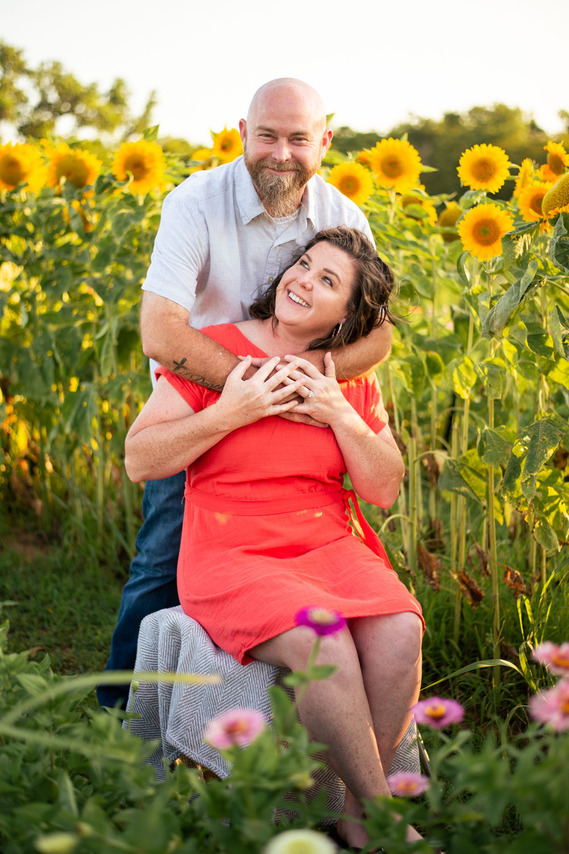 A husband and wife pose in front of a flower meadow at sunset in Oklahoma