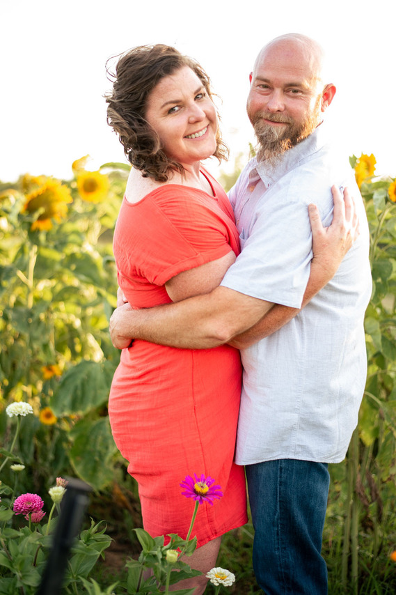 A husband and wife pose in front of a flower meadow at sunset in Oklahoma