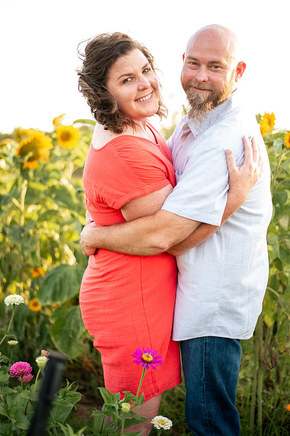 A husband and wife pose in front of a flower meadow at sunset in Oklahoma