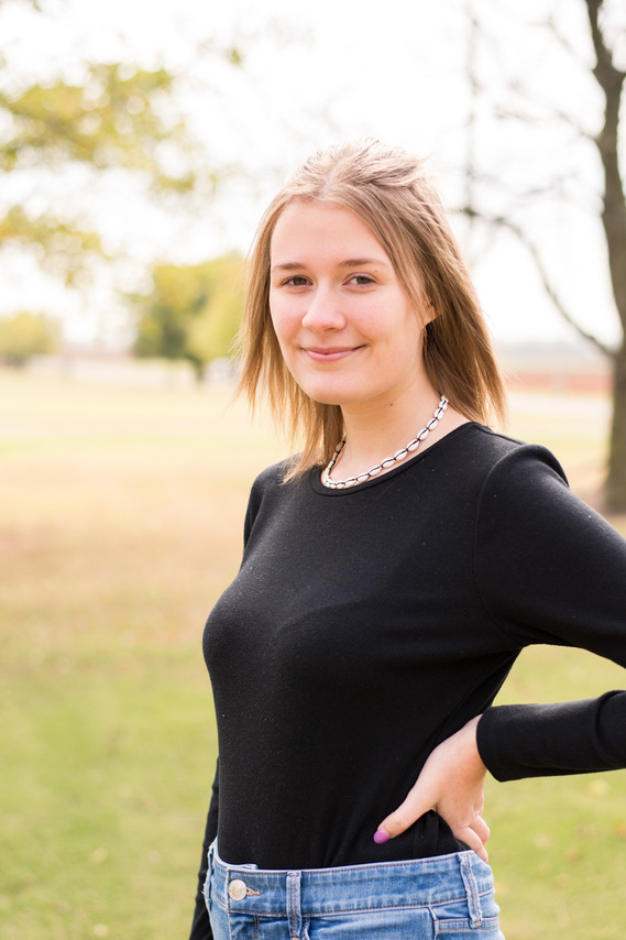Portrait of a teenage girl in a black shirt standing in a park with her hand on her hip