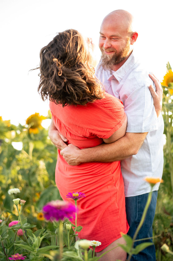A husband and wife pose in front of a flower meadow at sunset in Oklahoma