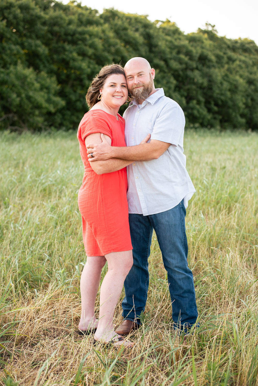 A husband and wife pose in front of a grassy meadow at sunset in Oklahoma
