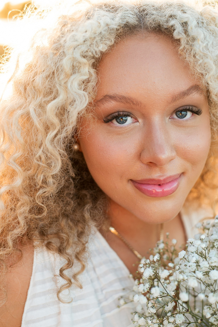close up portrait of a high school senior girl with blond curly hair and blue eyes smiling softly with bouquet of baby's breath flowers by her face at Martin Nature Park in Oklahoma City