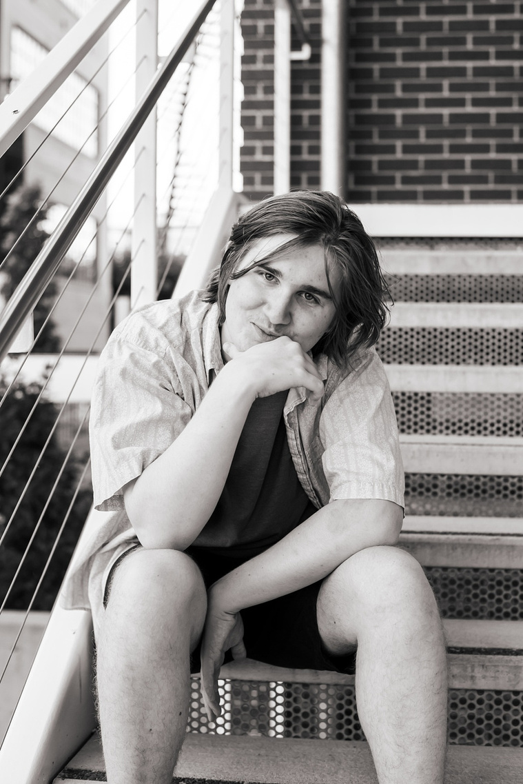 black and white portrait of a senior boy sitting on metal steps with one hand on his chain and softly smiling in midtown Oklahoma City