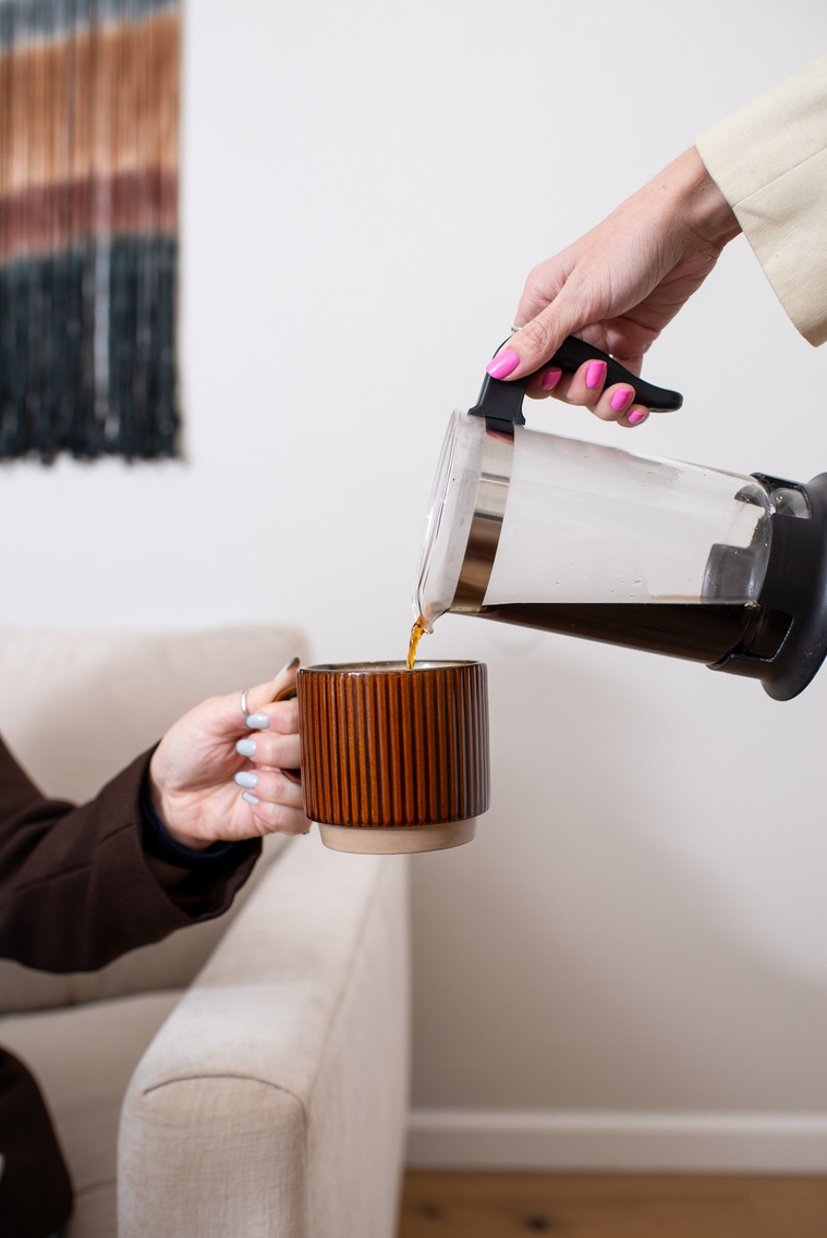 close up branding image of hands of one girl holding out her coffee cup while the hand of her business partner pours coffee into it 