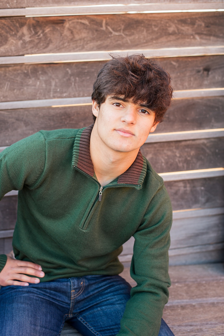 close up portrait of a hispanic high school senior boy wearing a green sweater and jeans sitting casually on the rooftop of Coffee Slingers in Automobile Alley in Oklahoma city