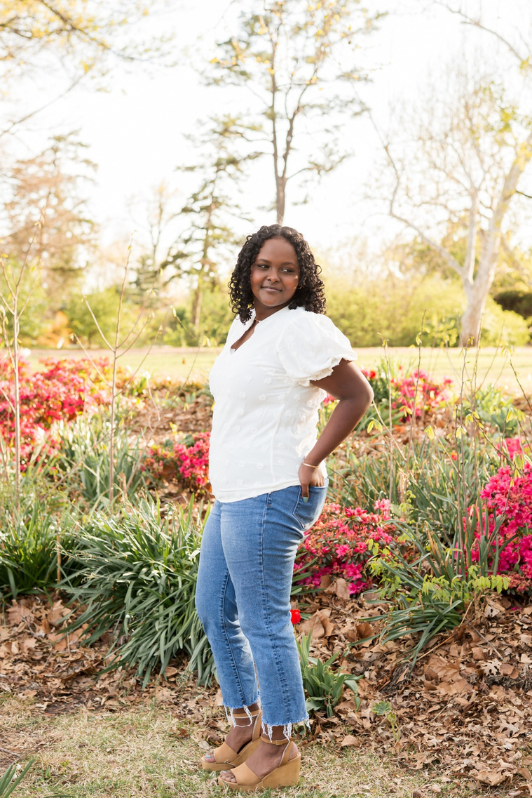senior girl wearing jeans and a white shirt stands among the flowers and trees of Will Rogers Gardens in OKC