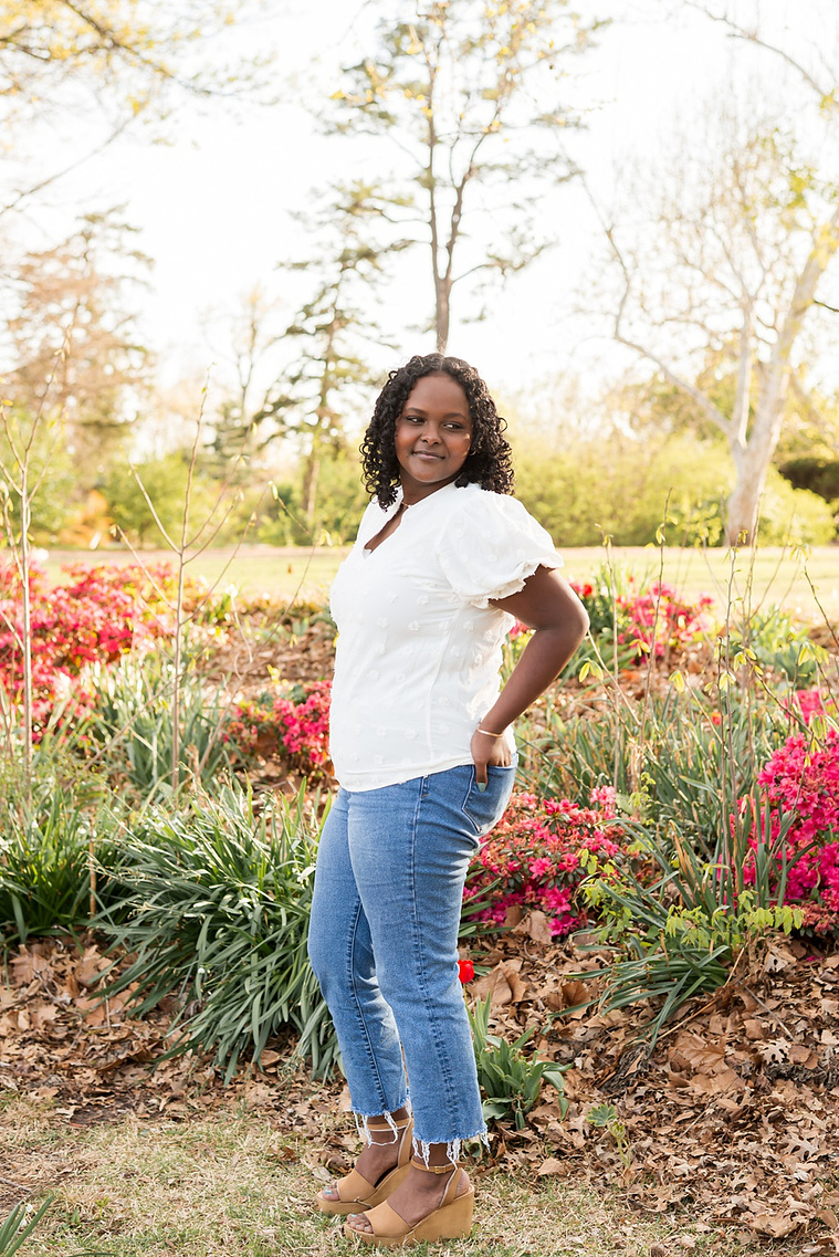senior girl wearing jeans and a white shirt stands among the flowers and trees of Will Rogers Gardens in OKC