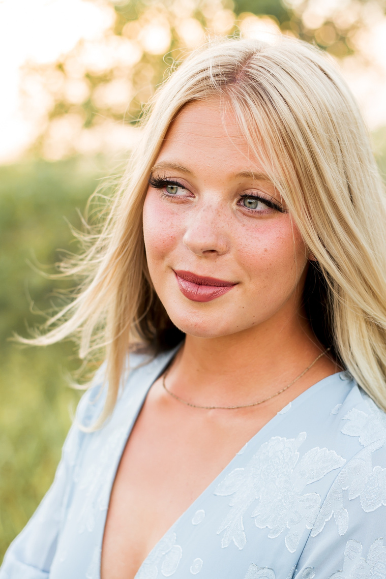 High school senior girl smiling softly and looking off camera in a field in central Oklahoma for her senior photos