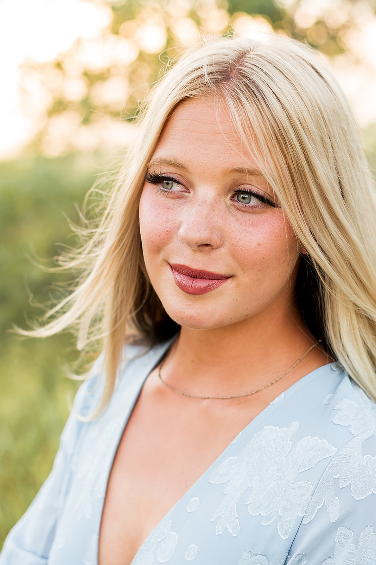 High school senior girl smiling softly and looking off camera in a field in central Oklahoma for her senior photos