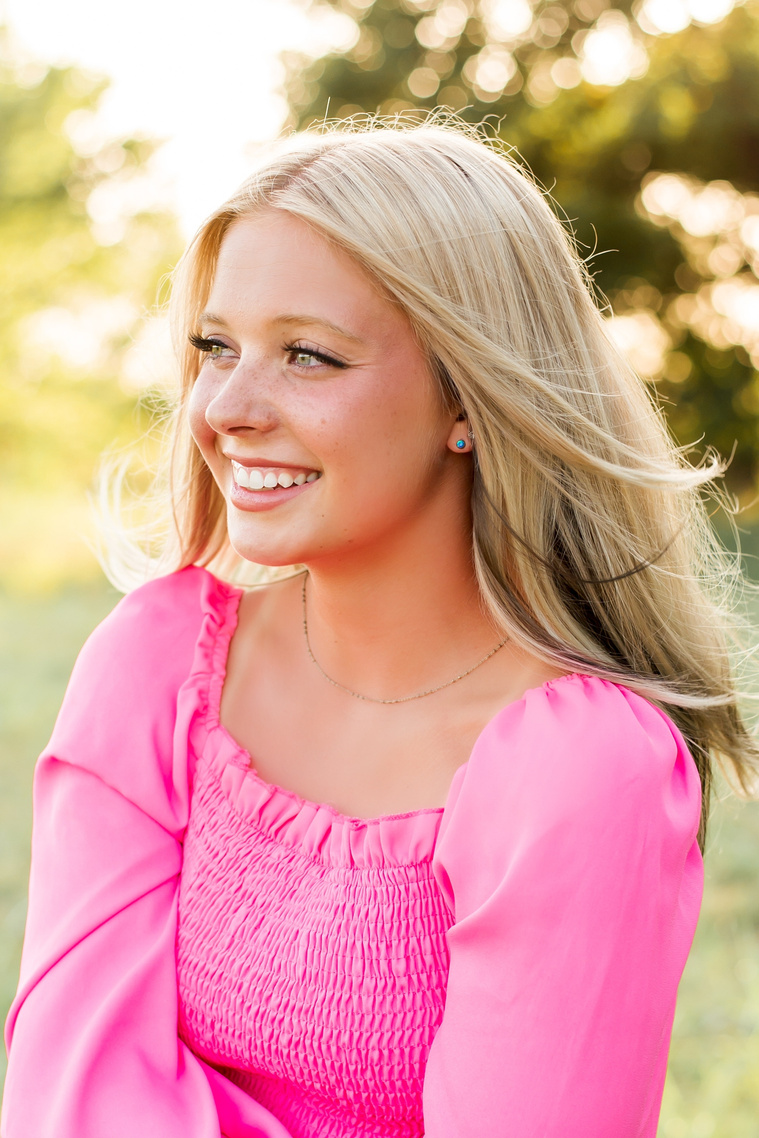 High school senior girl smiling beautifully and looking off camera in a field in central Oklahoma for her senior photos