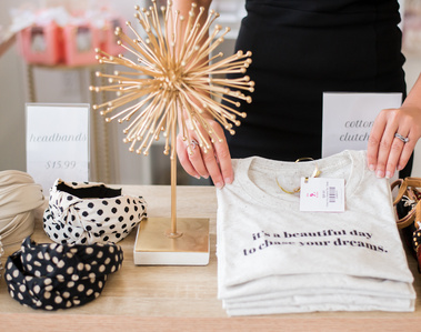 close up of a boutique owner's arms and hands as she places t-shirts on a table for sale amid other girly merchandise in Oklahoma City