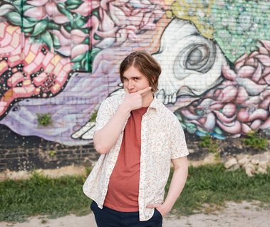 senior boy in a button down shirt making a funny dramatic face in front of a colorful wall mural in midtown Oklahoma City