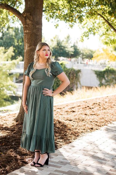 high school senior girl stands with hand on hip on a sidewalk in a green dress with trees behind her at Myriad Gardens in Oklahoma City