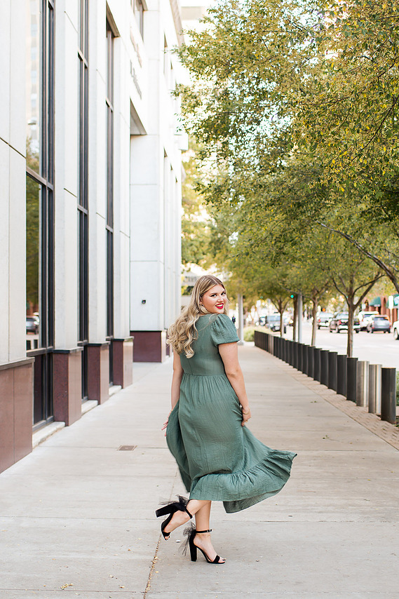 pretty senior girl wearing a green flowy dress laughs and twirls around on a sidewalk along a downtown OKC street