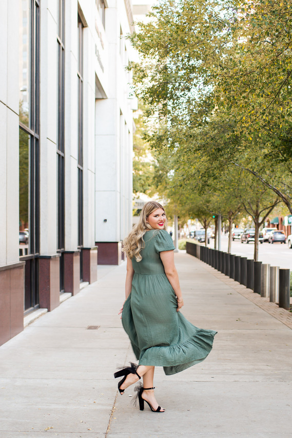 blond high school senior girl wearing a long green dress twirls on a sidewalk with black heels and smiles over her shoulder in downtown Oklahoma City