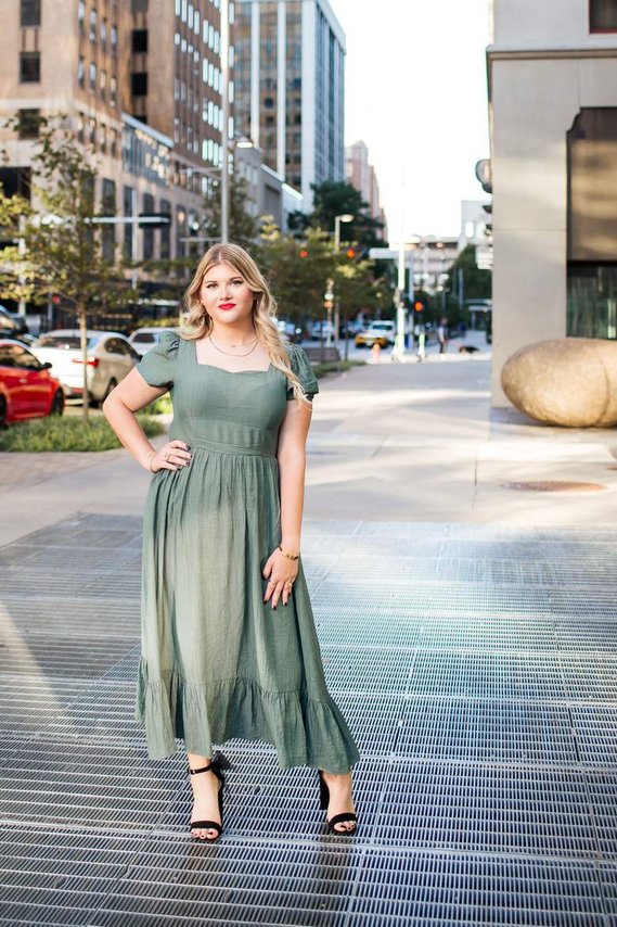 high school senior girl in a green dress and black heels stands and poses on a sidewalk in downtown Oklahoma City