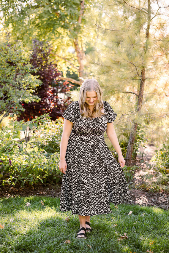blond high school senior girl wearing a long dress walks in the grass looking down and holding her skirt in the middle of Myriad Botanical Gardens in Oklahoma City