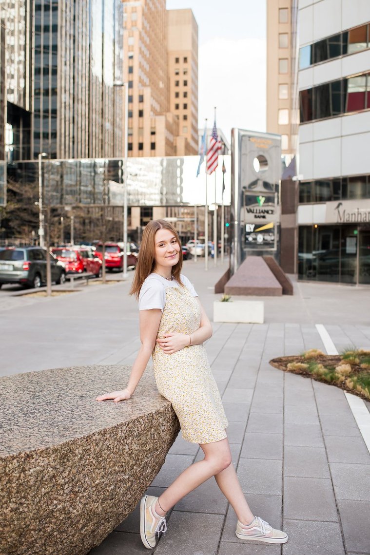 high school senior girl leans against a rock on the sidewalk near the Devon tower in downtown Oklahoma City