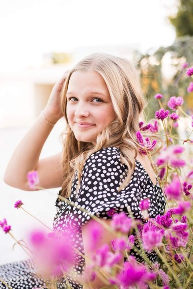high school senior girl sits among pink flowers with her hand in her hair in a dress and smiles softly at Myriad Gardens in Oklahoma City