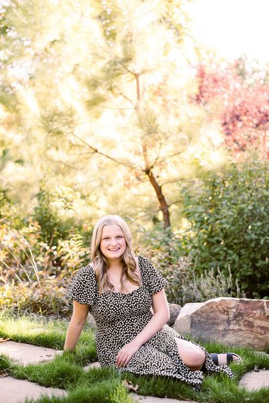 high school senior girl sits among the grass and stones in a dress and smiles with trees behind her at Myriad Gardens in Oklahoma City