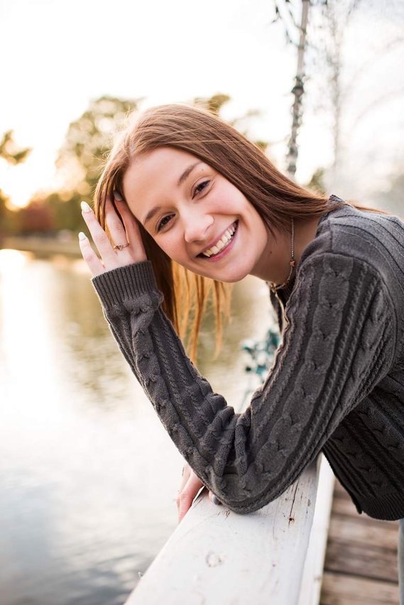 high school senior girl leans against a white bridge and smiles at Shannon Springs Park in Chickasha Oklahoma