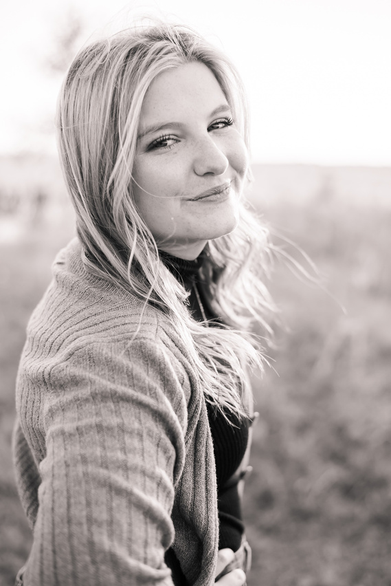 black and white photo of a high school senior girl standing to the side and looking at the camera with her hair blowing in the wind and smiling softly