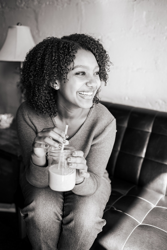 black and white portrait of an Ethiopian senior girl sitting on a couch in a coffee shop laughing to the side and holding her iced coffee drink in Norman Oklahoma