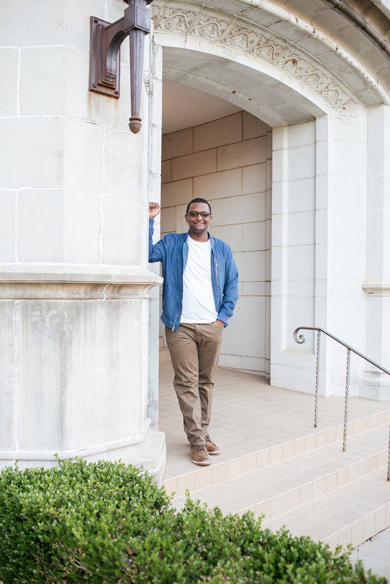 senior boy wearing a blue jacket, white t-shirt and khakis leans casually on his elbow and smiles in the outside entryway of the chemistry building on the OU campus in Norman, Oklahoma