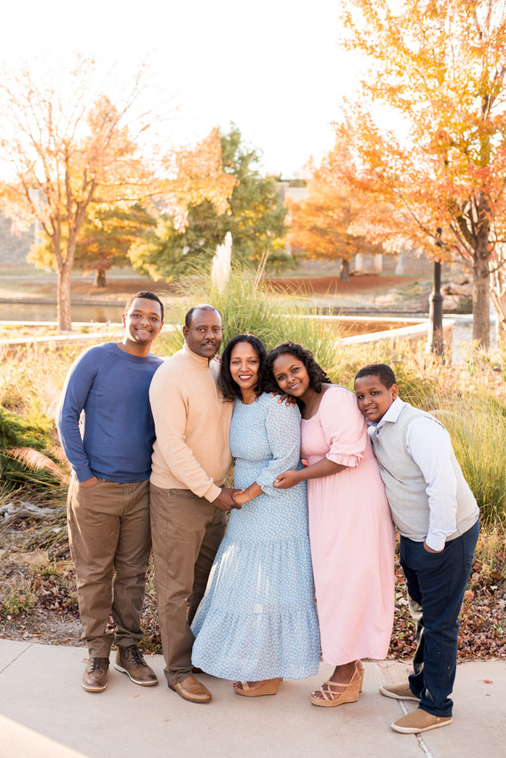 a mom and dad stand and hug their three teen kids in front of a park and fall trees in Oklahoma City