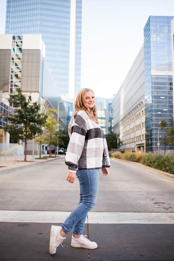 high school senior girl in a shacket and tennis shoes stands in a crosswalk with the devon buildings behind her in Oklahoma City 