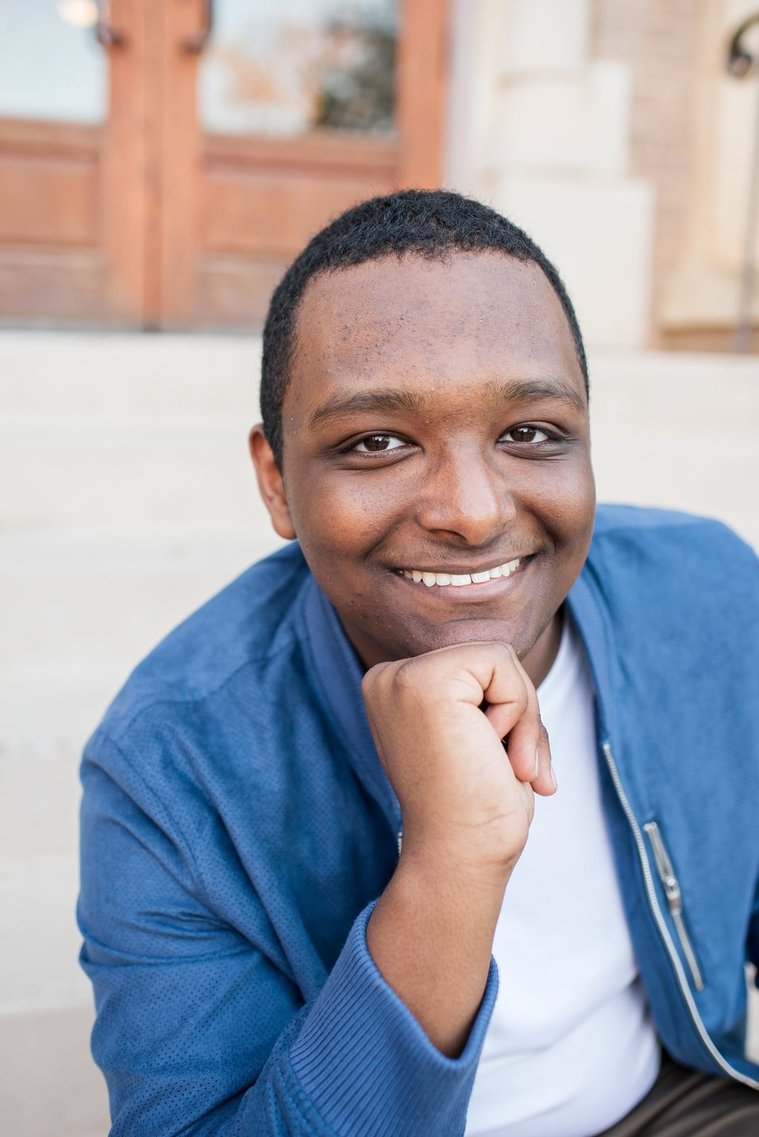 close up portrait of an african-american high school senior boy wearing a blue jacket and smiling on the steps of a building on the OU campus in Norman Oklahoma